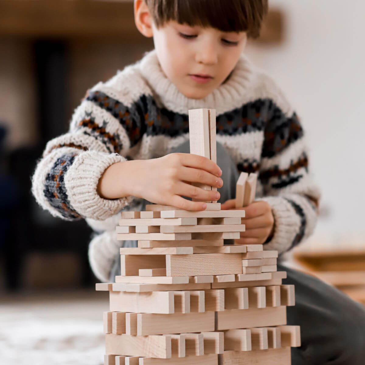 child playing with architectural wooden blocks by wooden story