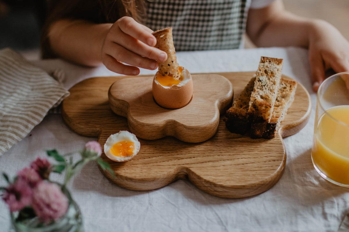 Child dipping a toast soldier into a soft-boiled egg served in a Blue Brontide solid oak egg cup and wooden breakfast set