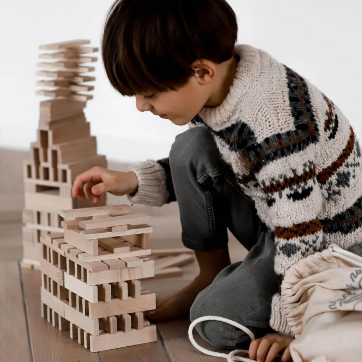 child playing with architectural wooden blocks by wooden story