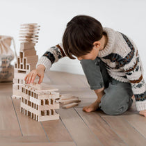 child playing with architectural wooden blocks by wooden story