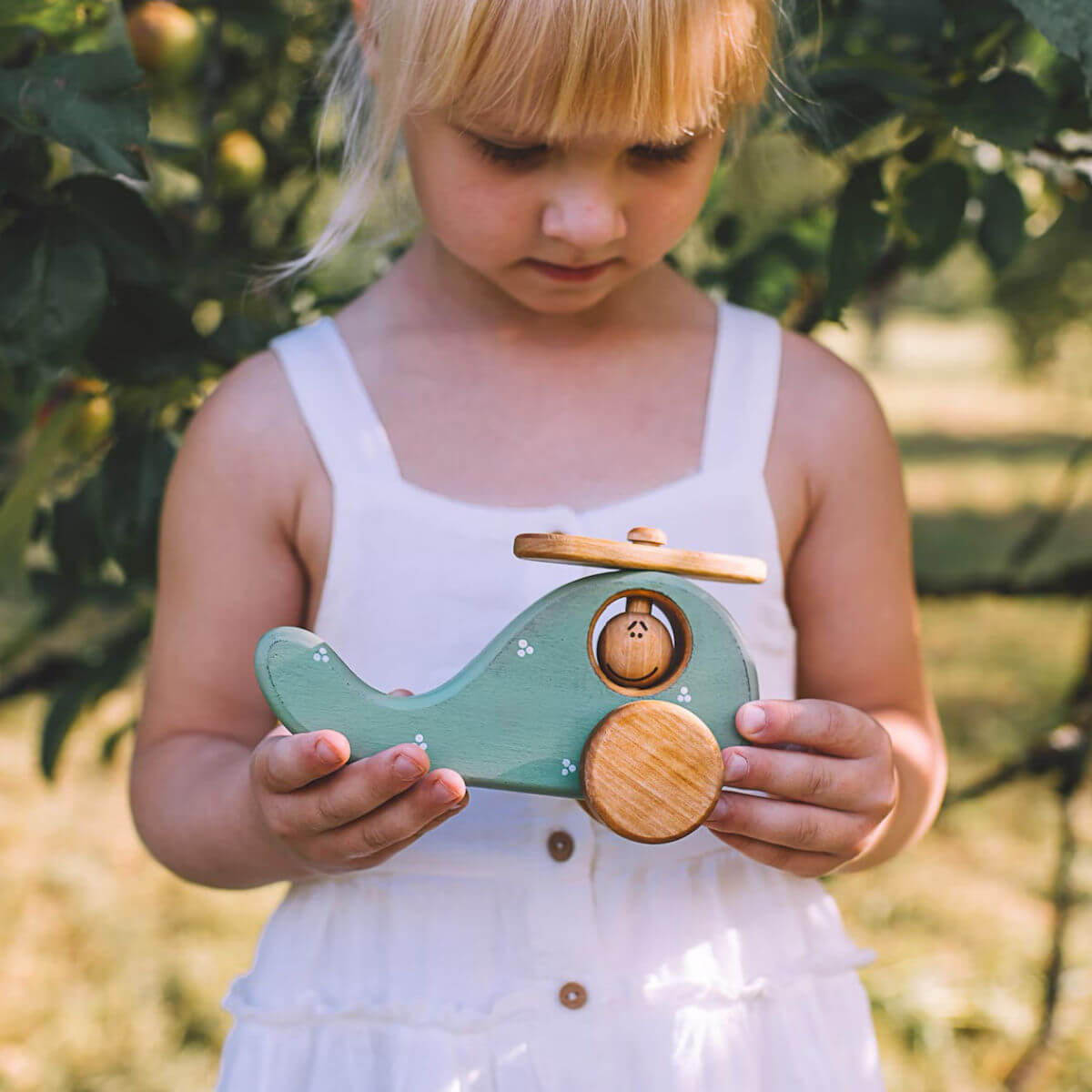 Young girl holding a wooden toy helicopter outdoors handmade by friendly toys