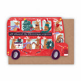 A Christmas-themed double-decker bus card or print featuring illustrated reindeer passengers, holiday decorations, and the text 'all aboard the Christmas express,' shown in front of a brown kraft envelope on a white background by sister paper co.