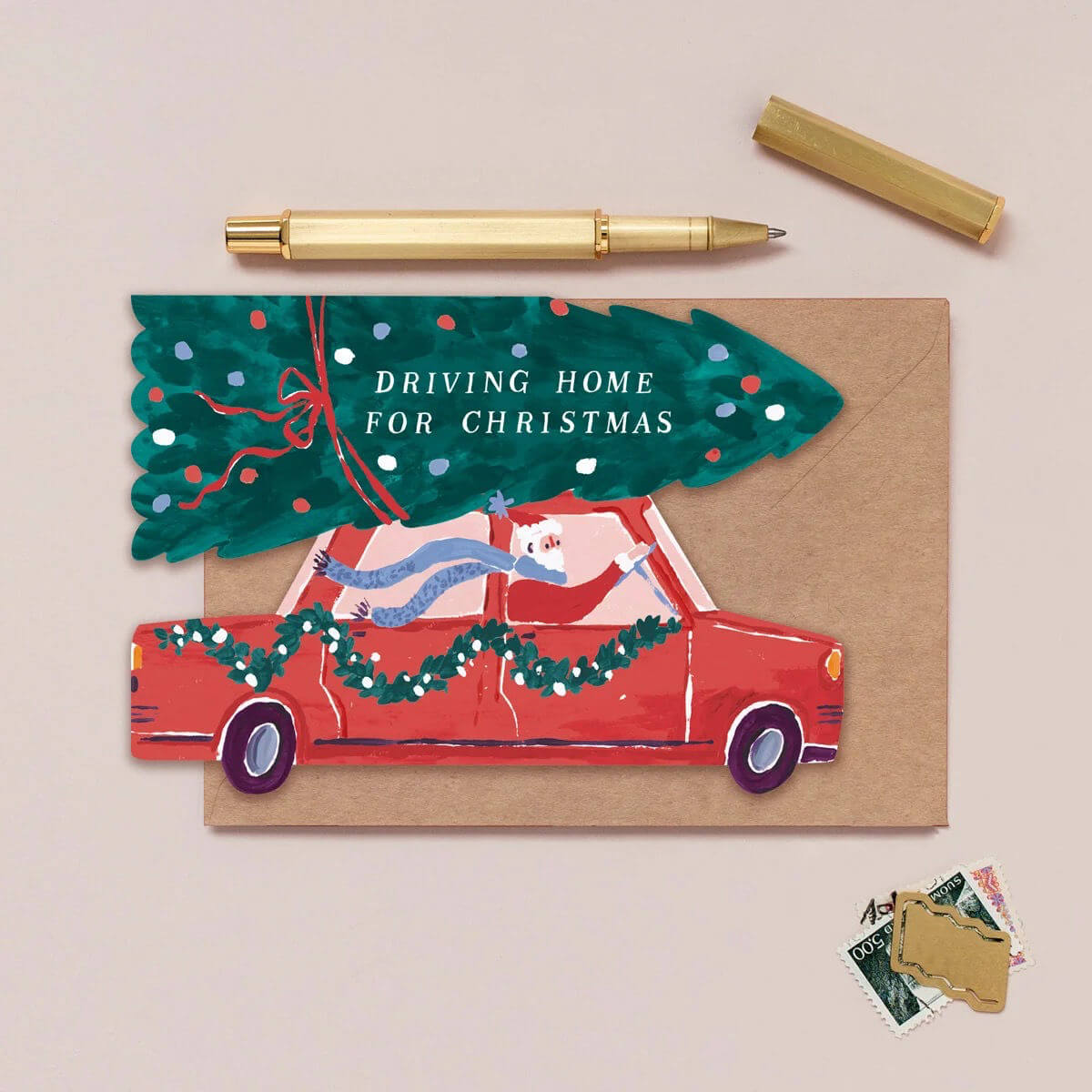 Sister Paper Co. illustrated Christmas greeting card with a red car and tree, featuring the text 'Driving Home for Christmas', on a beige background.