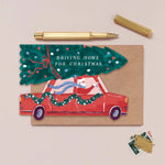 Sister Paper Co. illustrated Christmas greeting card with a red car and tree, featuring the text 'Driving Home for Christmas', on a beige background.